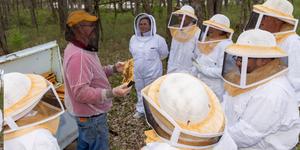 Man holding a bee comb showing a class of students in bee suites
