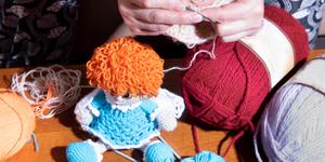 Close up of a woman crochetting a doll in a dress