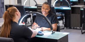 A young woman working on the nails of a client in a student salon
