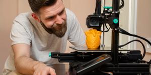A young man using a 3D Printer to make and orange owl.