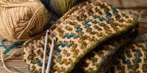 Some yard and needles resting on a piece of Tunisian crochet work