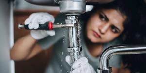 A woman under a sink with a wrench working on a leak.
