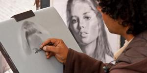 Someone drawing a life-like portrait with graphite on sketch pad.