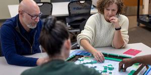 A group of two women and two men playing Mah Jongg in a classroom.